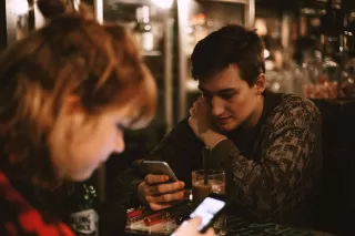 Couple at dinner, one distracted by phone while the other feels ignored, revealing social dynamics.