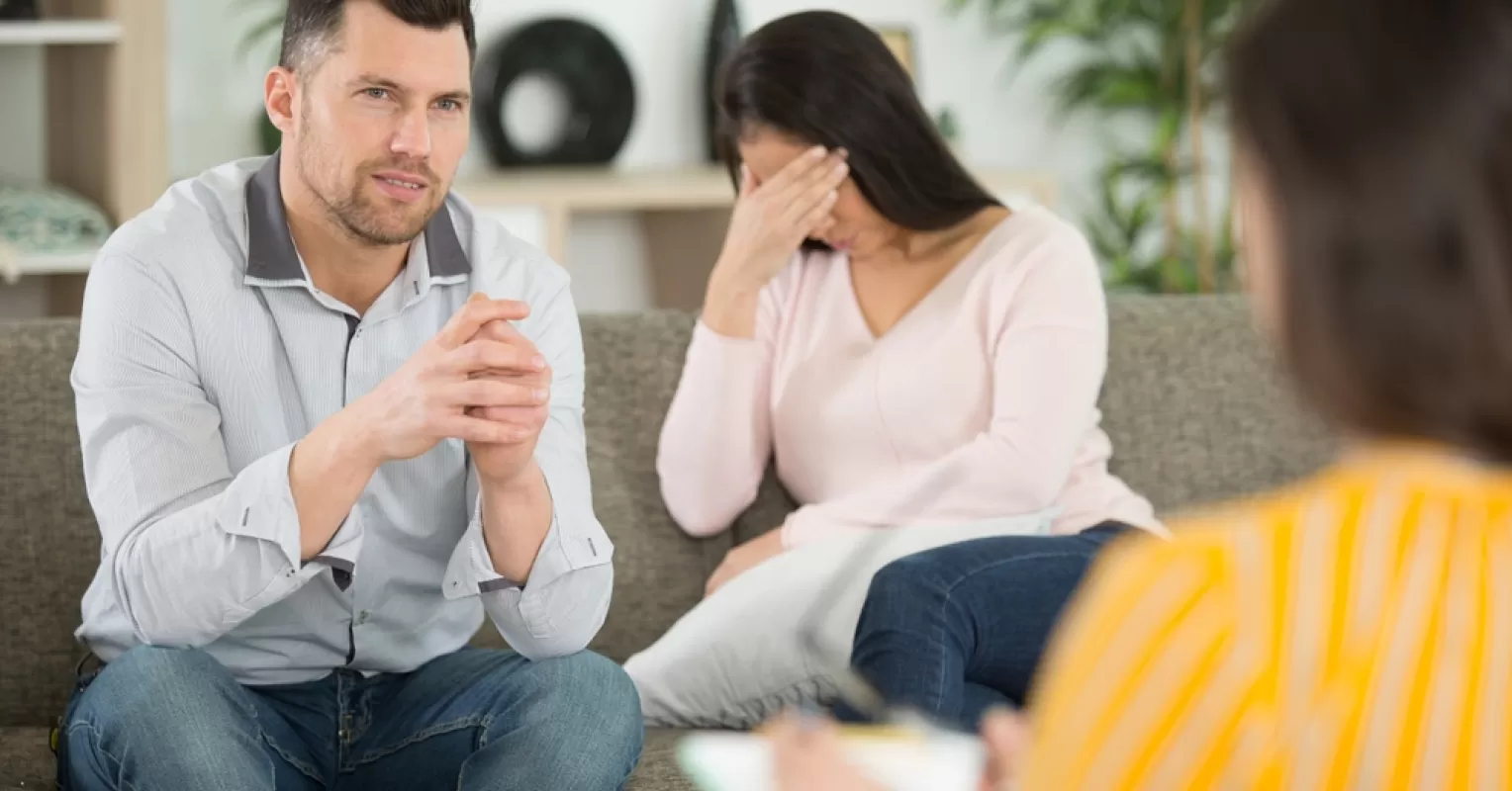 Couple sitting apart, showing signs of frustration in therapy session