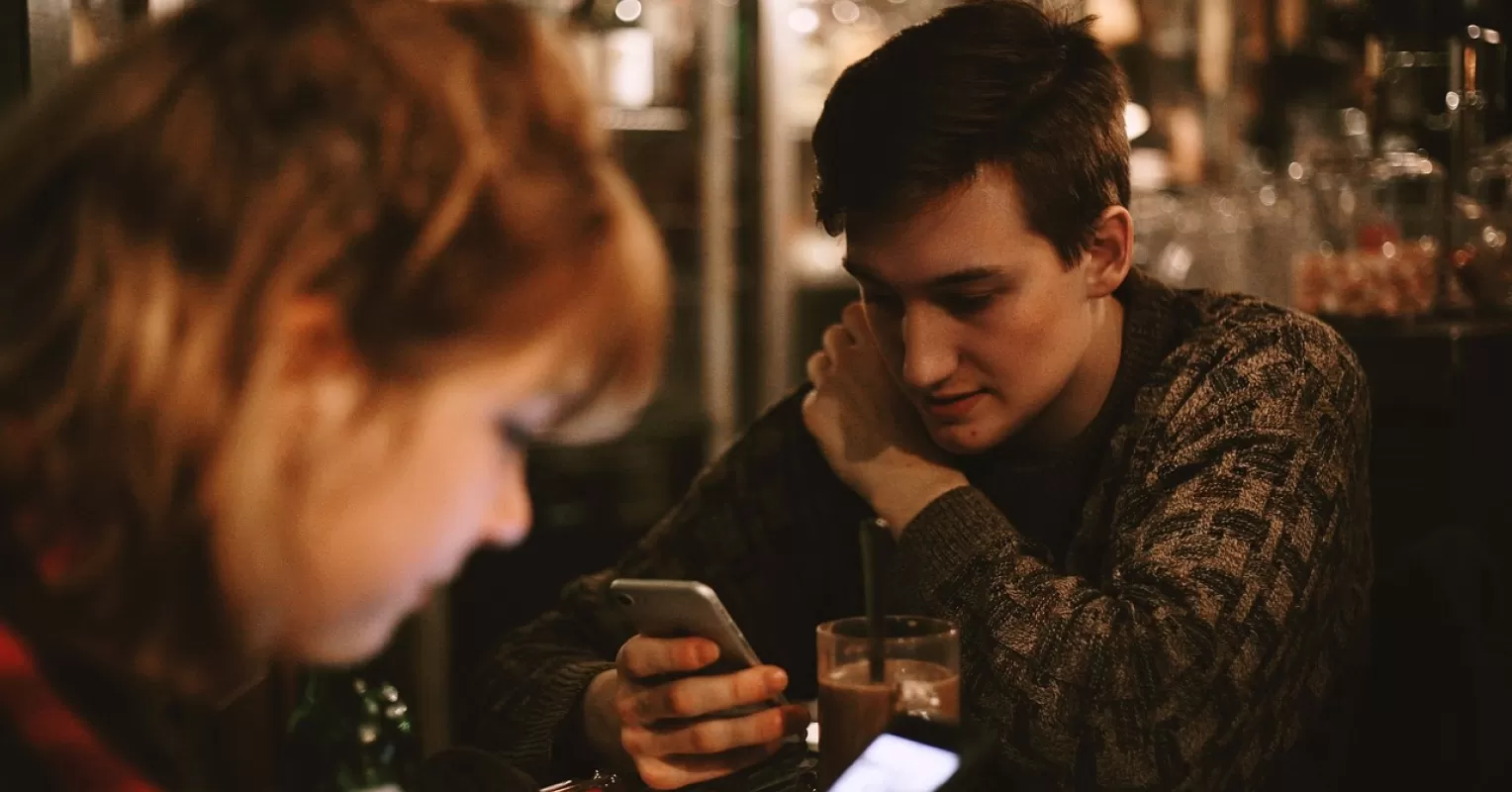 Couple at a restaurant, one partner focused on their phone instead of each other