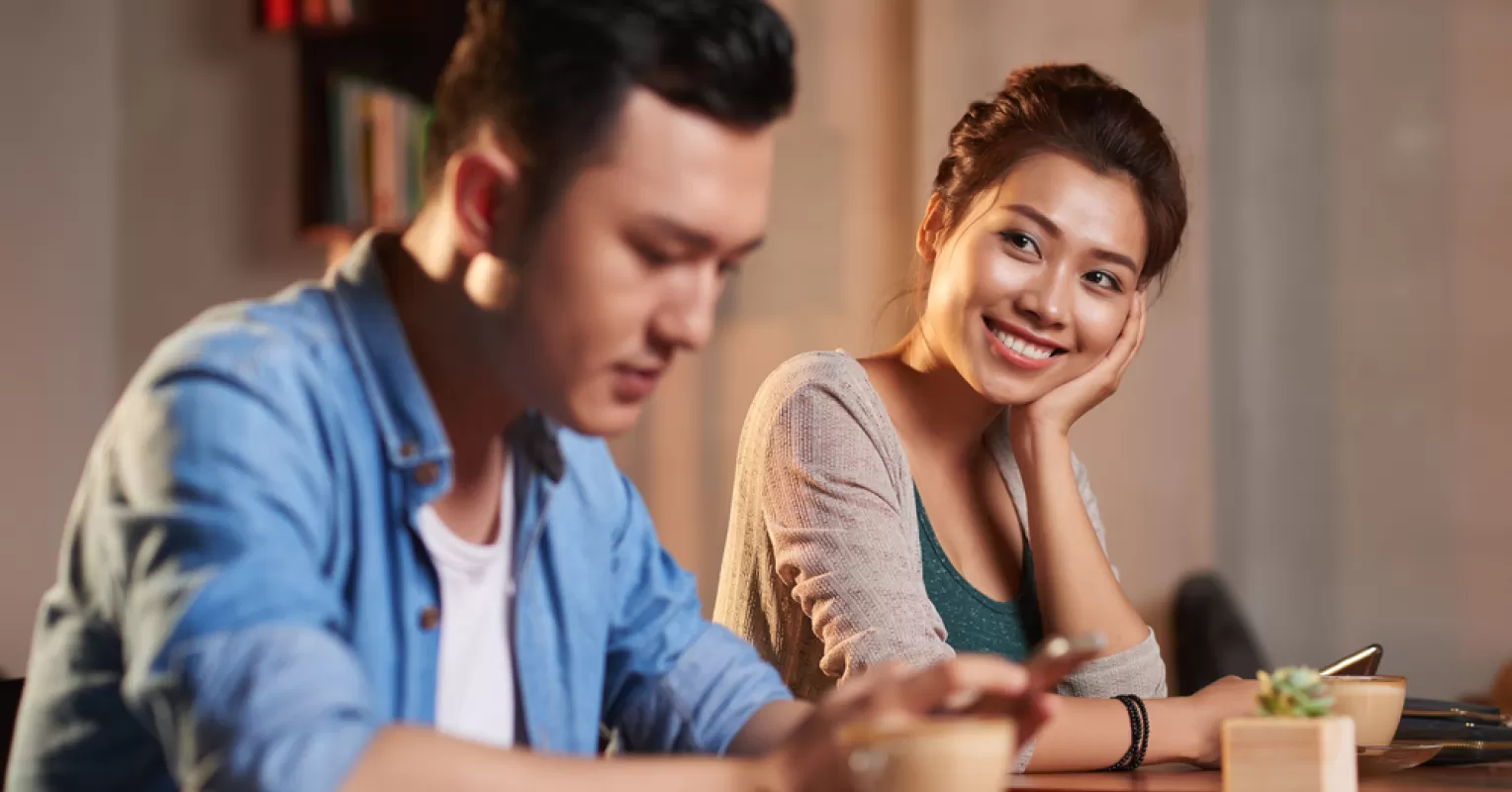 A person gazing thoughtfully at someone across a crowded room, feeling drawn to them.